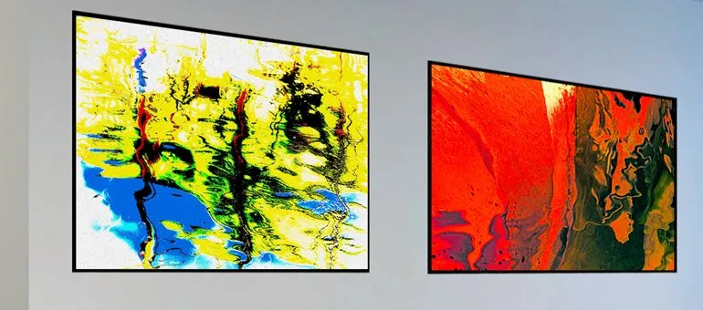 Two abstract paintings hang on a wall: one features vibrant yellow, blue, and green swirls, while the other displays bold orange and red hues.