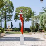 A sculpture of a woman in a flowing red dress, elegantly posed on a white pedestal.
